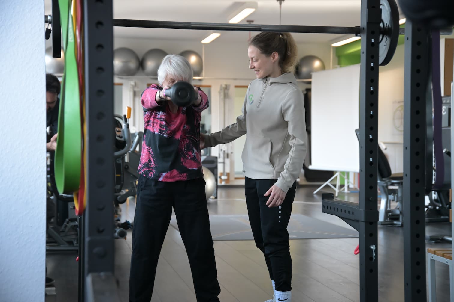 Eine Physiotherapeutin unterstützt ihre Patientin beim gezielten Krafttraining mit Gewichten und achtet dabei auf eine korrekte Ausführung.
